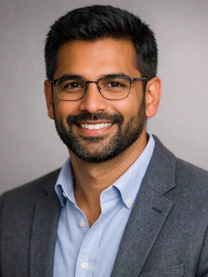 Portrait of a demo persona against a plain gray background, wearing a blazer over a light shirt, evenly lit, looking into the camera